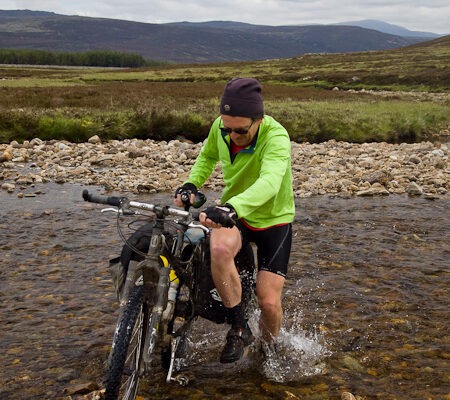 Image of Reuben hopping across the Geldie Burn (in the Cairngorms) to keep one foot dry!